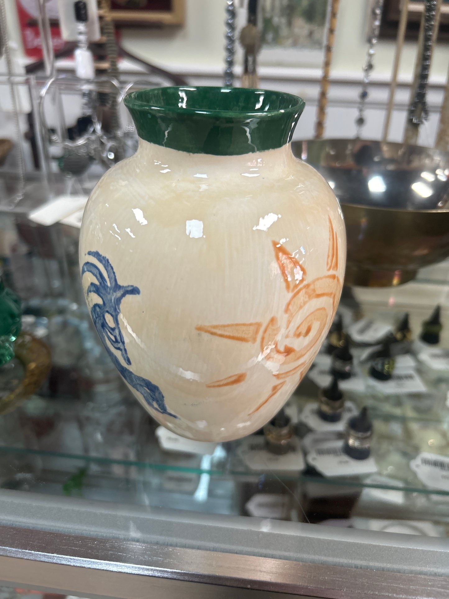 creamy-white ceramic vase features painted orange sun and blue spirit figure designs with a dark green rim