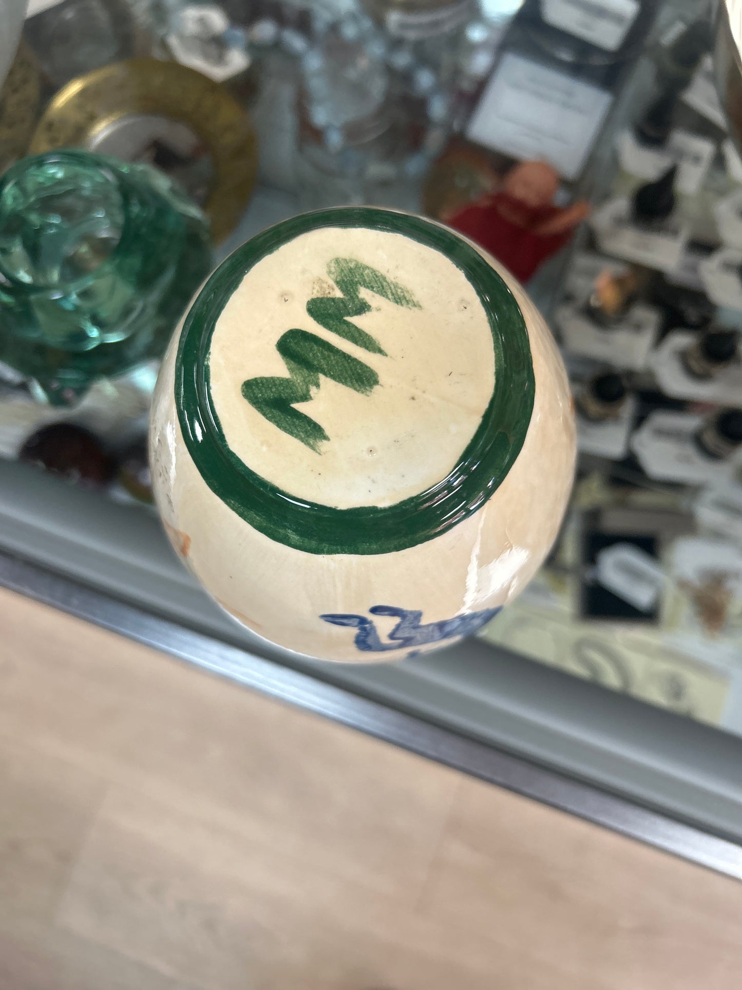 creamy-white ceramic vase features painted orange sun and blue spirit figure designs with a dark green rim